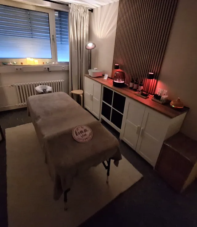 Der ganze Massageraum mit Liege, Sideboard und warmem Licht